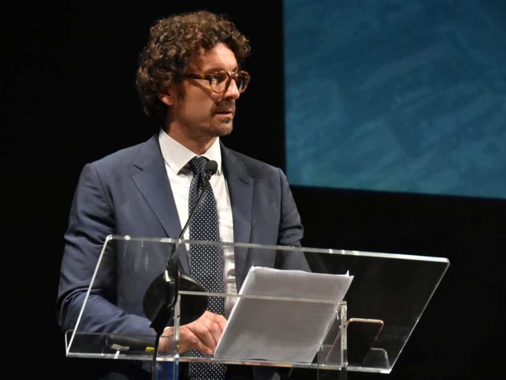 ------------------------------------------------------- Scavalco Porto Livorno e collegamenti ferroviari, firmato l'Accordo Scritto da Pamela Pucci, giovedì 23 maggio 2019 LIVORNO - Una firma che consentirà di collegare via ferro il Porto di Livorno e l'Interporto Vespucci di Guasticce, trasformando definitivamente l'Interporto in retro-porto, con evidenti vantaggi per l'intero sistema logistico e per l'economia toscana. E' quella posta questa mattina al Teatro Goldoni di Livorno dal presidente della Regione Toscana, dal Ministro delle infrastrutture, dall'amministratore delegato di Rete Ferroviaria Italiana, dal commissario straordinario dell'Autorità di Sistema Portuale del Mar Tirreno Settentrionale e dal presidente dell'Interporto Toscano Amerigo Vespucci, alla presenza dell'assessore regionale alle infrastrutture ed ai trasporti. L'intervento, che renderà finalmente possibile la realizzazione dello scavalco ferroviario della linea Tirrenica a Livorno, ha un costo complessivo di 27 milioni di euro e sarà realizzato grazie ad un finanziamento regionale da 20,2 milioni. Un investimento addirittura maggiore rispetto al contributo di 17 milioni precedentemente annunciato dalla stessa Regione Toscana. Grazie all'incremento dei fondi regionali, ai contributi di 4,3 milioni da parte di RFI (Contratto di Programma 2017-2021) e di 2,5 milioni del Ministero delle infrastrutture e dei trasporti, a Livorno verrà realizzato un ulteriore tratto di binario, lungo circa 1,5 km (circa 360 metri del quale realizzati su un viadotto costituito da 15 campate), che sovrappasserà la linea ferroviaria Tirrenica Pisa-Roma nell'ambito della stazione di Livorno Calambrone. In vista della realizzazione dello scavalco, con la firma dell'accordo l'Autorità di sistema portuale si impegna a favorire, nella misura più ampia possibile, l'integrazione tra il Porto di Livorno e l'Interporto Vespucci ed a contribuire all'aumento dei traffici via ferro da e per il porto (con lo scopo di raggiungere gli obiettivi fissati dalla Comunità Europea di trasferire su ferro entro il 2030 il 30% degi traffici merci con percorrenze superiori ai 300 km, ed il 50% entro il 2050). L'Interporto Toscano Vespucci si impegnerà, invece, a supportare RFI per la progettazione, le espropriazioni necessarie e la realizzazione dello scavalco ferroviario. L'accordo sottoscritto oggi, però, non tratta solo dello scavalco di Livorno, ma fissa azioni e competenze dei soggetti firmatari per la realizzazione di altre tre opere ferroviarie collegate tra loro dal progetto di spostare su ferro buona parte del traffico merci in arrivo in Toscana, potenziando l'attuale dotazione infrastrutturale i modo da collegare meglio il sistema dei porti toscani al corridoio ferroviario europeo scandinavo-mediterraneo. Le altre opere previste dall'accordo sono: - il collegamento ferroviario fra l'interporto Vespucci e le linee Collesalvetti-Vada e Pisa-Firenze (tramite bypass di Pisa): l'accordo riguarda il Progetto di fattibilità tecnica ed economica, che sarà redatto da RFI e condiviso tra le parti, valutando più alternative progettuali. - l'adeguamento a sagoma PC/80 di tutte le gallerie dell'Appennino tosco-emiliano presenti lungo la linea ferroviaria Prato-Bologna: si tratta di un'opera che Rete Ferroviaria Italiana ha iniziato e portato avanti nel 2018, con adeguamento delle gallerie allo standard P/C-80 (un ampliamento delle dimensioni delle gallerie per rendere possibile il passaggio di carri merci più larghi e capienti oltre che dei tir trasportati su ferro). Il termine dei lavori è previsto nell'arco di tre anni. Questo intervento risulta necessario anche come upgrade del Corridoio merci europeo scandinavo-mediterraneo. - la revisione dei collegamenti ferroviari per il porto di Piombino. L'Autorità di Sistema Portuale e RFI si sono impegnate a collaborare per definire la proposta di allaccio ferroviario più adatta a servire i volumi ferroviari del